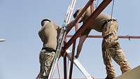 Zwei Soldaten demontieren auf einem Container einen Kabelschacht. Einer von ihnen steht auf einer Leiter am Metallgestänge