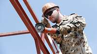 Ein Soldat steht an einem Metallgestänge und durchtrennt das Metall mit einem Trennschleifer