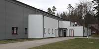 Eine grauer, moderner, hallengroßer Flachbau mit wenigen Fenstern und kleineren, weißen Anbauten