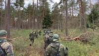 Mehrere Soldaten laufen in zwei Reihen hintereinander durch einen Wald.