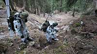 In einem sehr steilen Waldstücks seilen sich Soldaten mithilfe eines Seiles ab.
