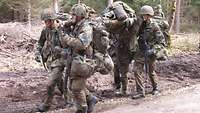 Vier Soldaten tragen auf ihren Schultern eine Trage, auf der ein Verwundeter liegt.