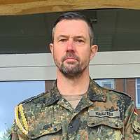 Ein Soldat mit Bart schaut direkt in die Kamera.