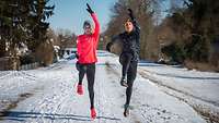 Eine Frau und ein Mann in Sportkleidung beim Hopserlauf auf einem verschneiten Weg