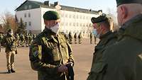 Drei Soldaten stehen sich gegenüber. Im Hintergrund stehen viele Soldatinnen und Soldaten angetreten. 