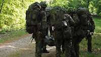 Vier Soldaten heben im Wald eine Trage mit einem Verwundeten hoch.