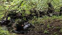 Vier Soldaten waten mit Marschgepäck durch die Uferzone eines Gewässers.