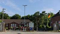 Die Hauptwache Eine zweispurige Straße führt zu einer Einfahrt mit Schranken und einem Wachhaus.