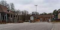 Eine zweispurige Straße führt zu einer Einfahrt mit Schranken und einem Wachhaus.