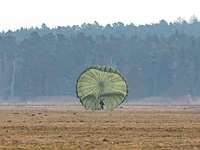 Fallschirmjäger mit Rundkappe T19 Fallschirm auf Wiese Ein Mensch steht vor einem aufgeblähten Fallschirm auf einer Wiese