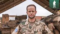 Portraitbild eines Soldaten. Hinter ihm stehen zwei Gefechtsfahrzeuge unter einer Zelthalle