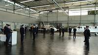 In einem Hangar sind Soldaten mit großem Abstand angetreten. Im Hintergrund stehen zwei Flugzeuge.