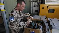 Ein Soldat steht an einem Tisch und packt Spanngurte in einen Karton