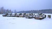 Mehrere Soldatinnen und Soldaten stehen neben sieben Panzern in der schneebedeckten Landschaft