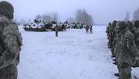 Viele Soldatinnen und Soldaten stehen angetreten vor einem Soldaten. Im Hintergrund stehen mehrere Panzer