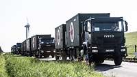 A long line of Military Trucks with Red Cross symbols on a Street