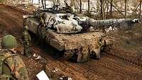 Ein Kampfpanzer steht auf einem Waldweg und wird von einem Soldaten betankt. Zwei weitere Soldaten beobachten den Tankvorgang