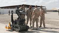 Ein estnischer Soldat unterhält sich mit vier belgischen Soldaten vor einem Roboter zur Kampfmittelräumung. 