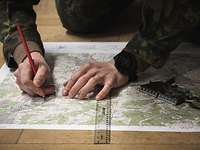Die Missionsplanung Ein Soldat kniet über einer Landkarte und zeichnet mit Kompass, Lineal und Bleistift auf ihr