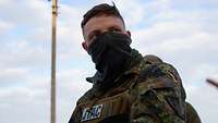 Ein deutscher Offizier steht vor einem leicht bewölkten Himmel 