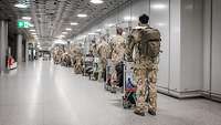 Viele Soldaten stehen mit ihrem Gepäck hintereinander in der Abfertigungshalle eines Flughafens