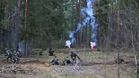 In einem Waldstück stehen oder liegen mehrere Soldaten in Stellungen