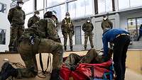 Ein Soldat liegt Probe in einem Rettungstuch, die anderen Teilnehmenden stehen um ihn herum. Zwei erklären das Material.