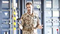 Ein Soldat steht vor Containern und spricht