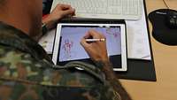 Ein Soldat wird beim Zeichnen auf einem Tablet über die Schulter gesehen