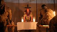 Gottesdienst: Der Militärseelsorger steht vor einem Altar, auf dem zwei Kerzen stehen. Mehrere Soldaten sitzen ihm gegenüber