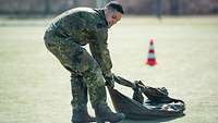 Ein Soldat zieht einen schweren Gegenstand übers Gras und läuft damit rückwärts