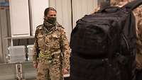 Im Vordergrund ein Soldat mit Rucksack, im Hintergrund steht eine Soldatin