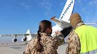 Eine Soldatin und ein Soldat stehen vor dem Flugzeug Antonow. Die Soldatin zeigt mit dem Finger auf das Flugzeug 