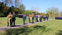 Soldaten gehen mit Kränzen auf einem Weg.