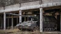 In einer alten Fahrzeughalle aus Beton steht eine Panzerhaubitze.
