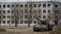 Vor einem großen verlassenen Wohngebäude steht ein Panzer.