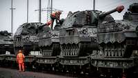 Mehrere Panzer sind auf Bahnwaggons verladen und stehen hintereinander auf einem Gleisabschnitt.