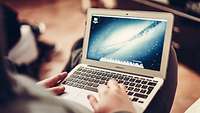 Eine Person hält einen Laptop auf seinem Knie.