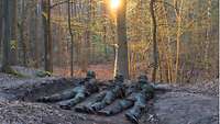 Drei Soldaten liegen auf dem Boden im Wald und beobachten das Gelände vor ihnen.
