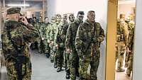 Viele Soldatinnen und Soldaten stehen mit Tarnschminke im Gesicht in Uniform mit ihren Waffen vor der Waffenkammer.