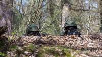Zwei Soldaten liegen in einer Stellung Wald am Boden und beobachten durch die Zielvisiere ihrer Gewehre das Gelände vor sich.