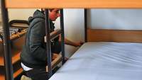 Ein junger Mann bezieht sein Bett mit Bettwäsche.