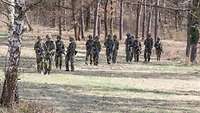 Soldatinnen und Soldaten laufen durch einen Wald.