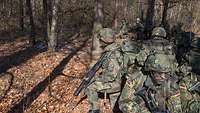 Soldaten knien im Wald und sichern sich gegenseitig in alle Richtungen ab.