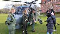 Zwei Soldatinnen und ein Soldat stehen vor einem Hubschrauber. Ein Filmteam interviewt sie.