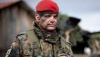 Ein Soldat mit rotem Barett hat einen Gefechtshelm, ein Funkgerät und ein Fernglas bei sich.