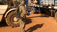 Zwei Soldaten und ein einheimischer Zivilist nehmen Ware auf einem Lkw an. Ein Soldat überprüft die Waren anhand einer Liste 