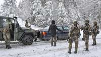 Soldaten und ein Zivilist stehen neben zwei Fahrzeugen, die auf einer verschneiten Straße dicht hintereinander stehen.