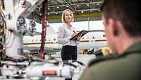 Eine Frau steht in einer Halle vor einem weißen Flugzeug und schaut in die Kamera.