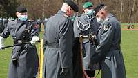 Vier Soldaten stehen um eine gesenkte Truppenfahne. Ein Soldat bringt ein Fahnenband an.